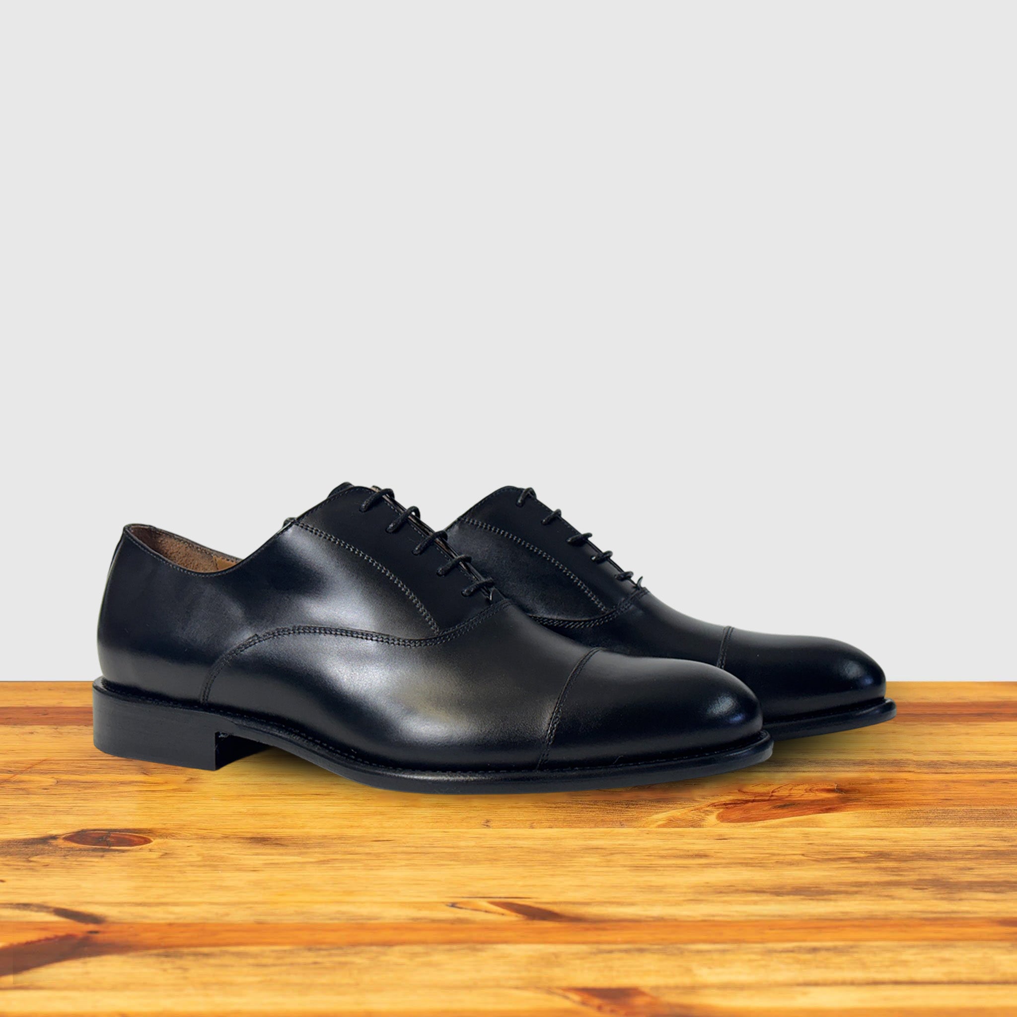 A Pair of Black leather dress shoe on a wooden surface with a light gray background