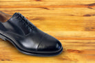 Black leather dress shoe on a wooden surface