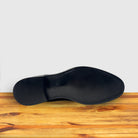 Outsole of Black leather dress shoe on a wooden surface with a light gray background