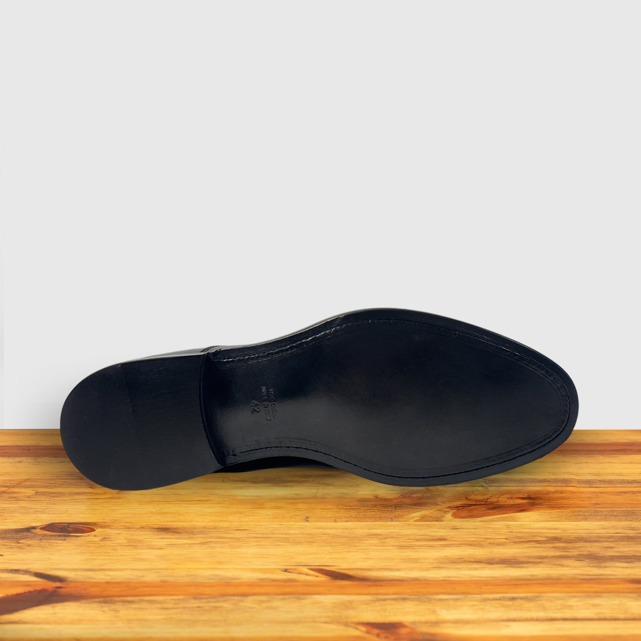 Outsole of Black leather dress shoe on a wooden surface with a light gray background