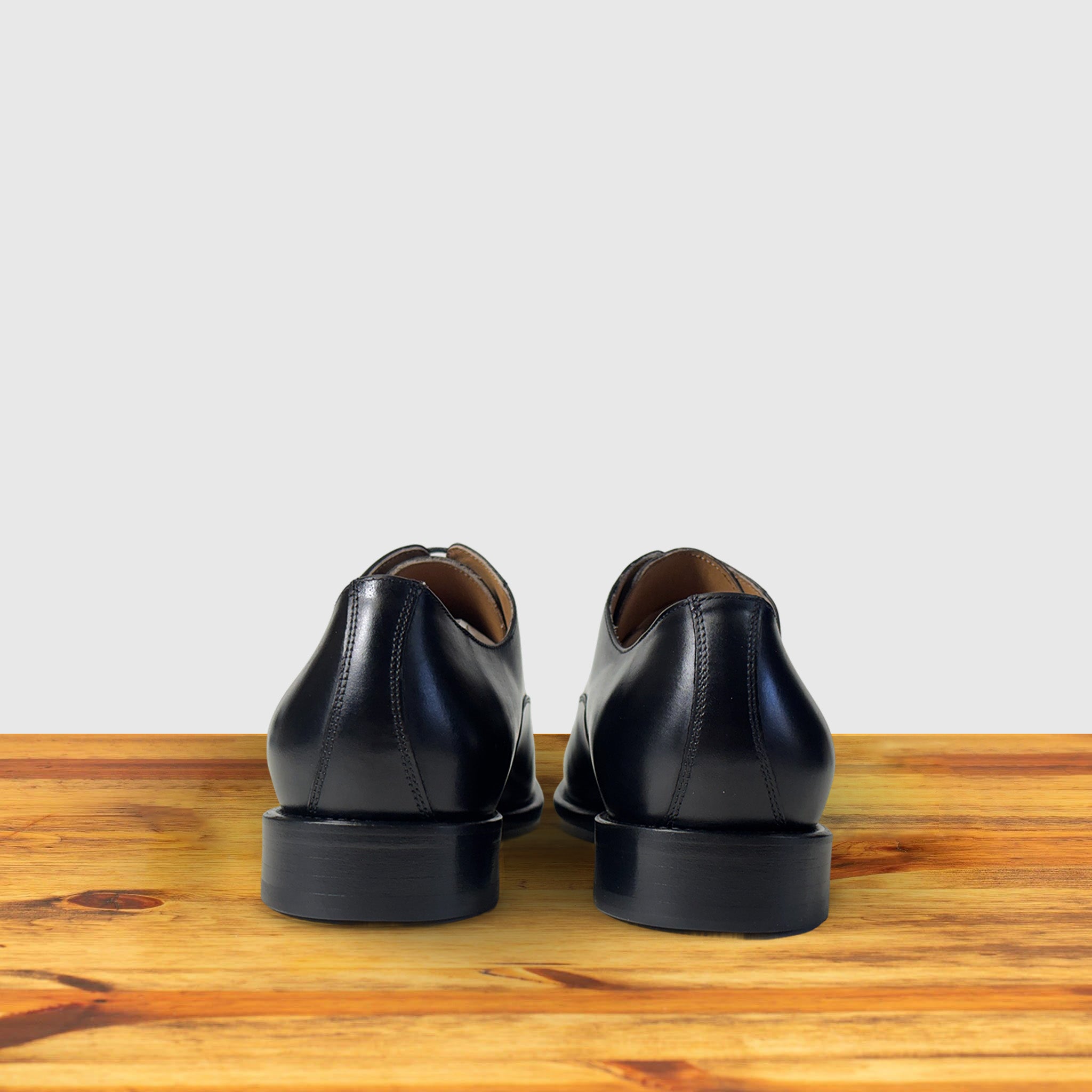 Black leather dress shoe on a wooden surface with a light gray background