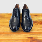 A pair of Black leather dress shoe on a wooden surface with a light gray background