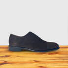 A Charcoal suede Oxford cap-toe shoe with a leather sole, displayed on a wooden surface.