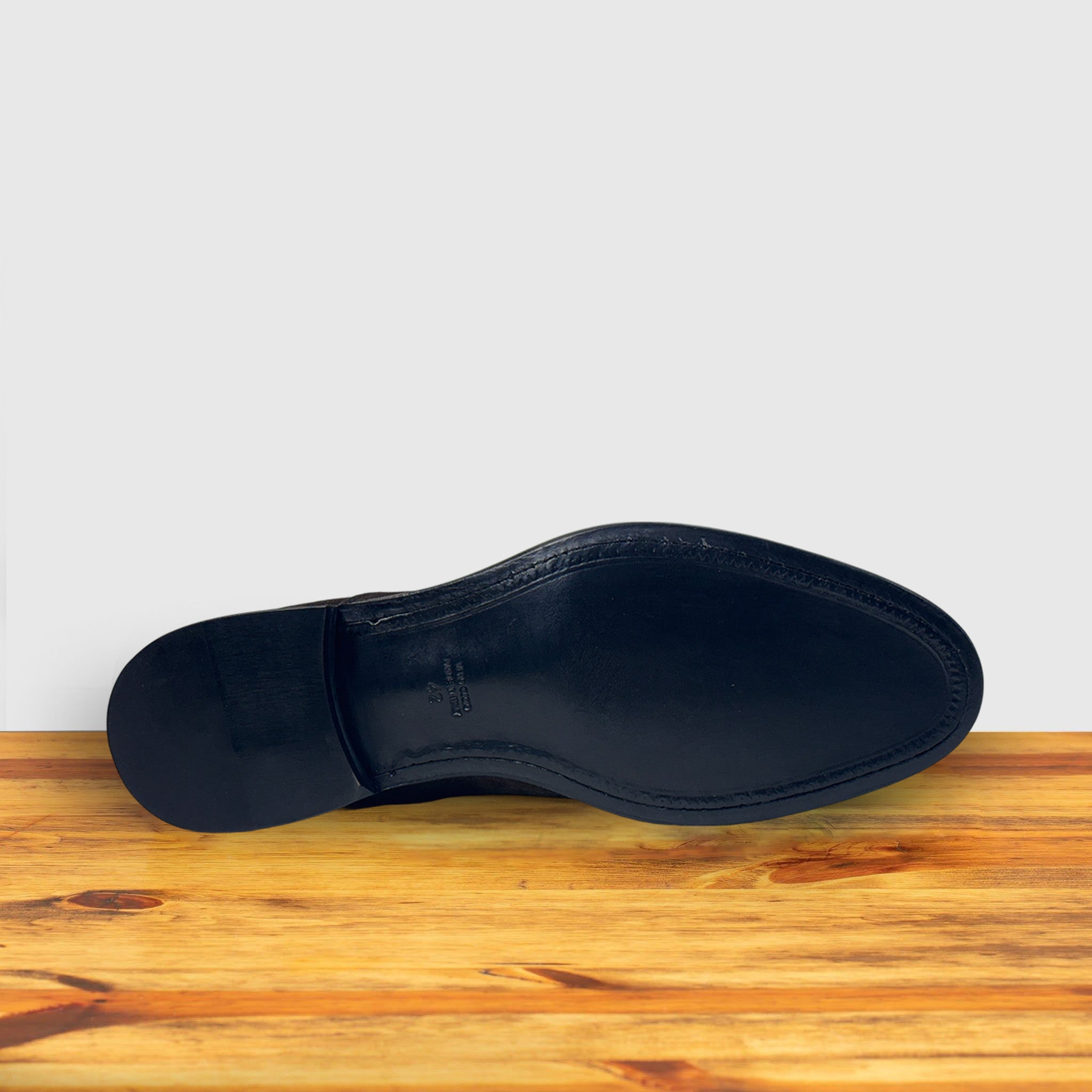 Outsole of  Charcoal suede Oxford cap-toe shoe with a leather sole, displayed on a wooden surface.