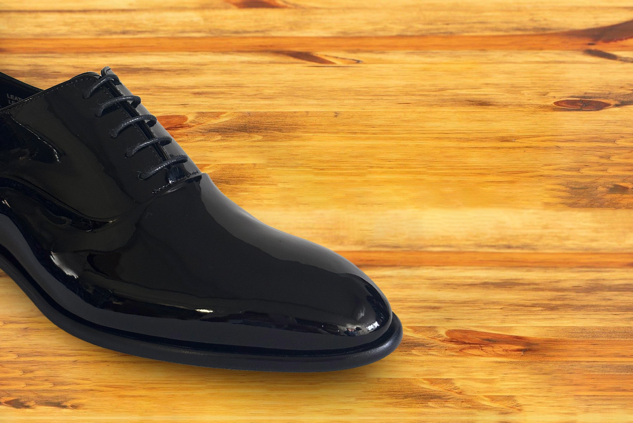 Black patent leather dress shoe on a wooden surface 