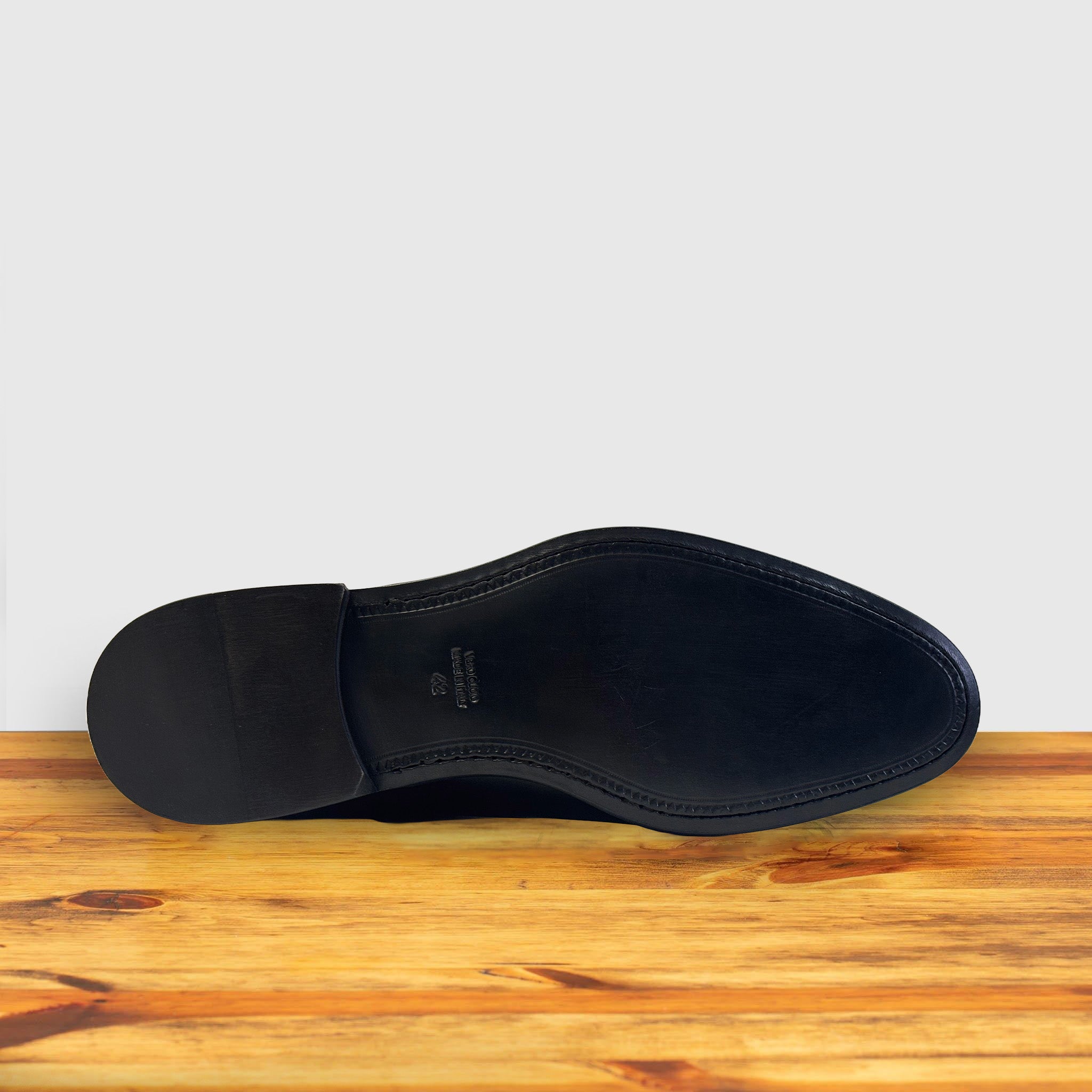 Outsole of Black patent leather dress shoe on a wooden surface with a light gray background