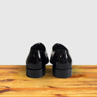 A Pair of Black patent leather dress shoe on a wooden surface with a light gray background