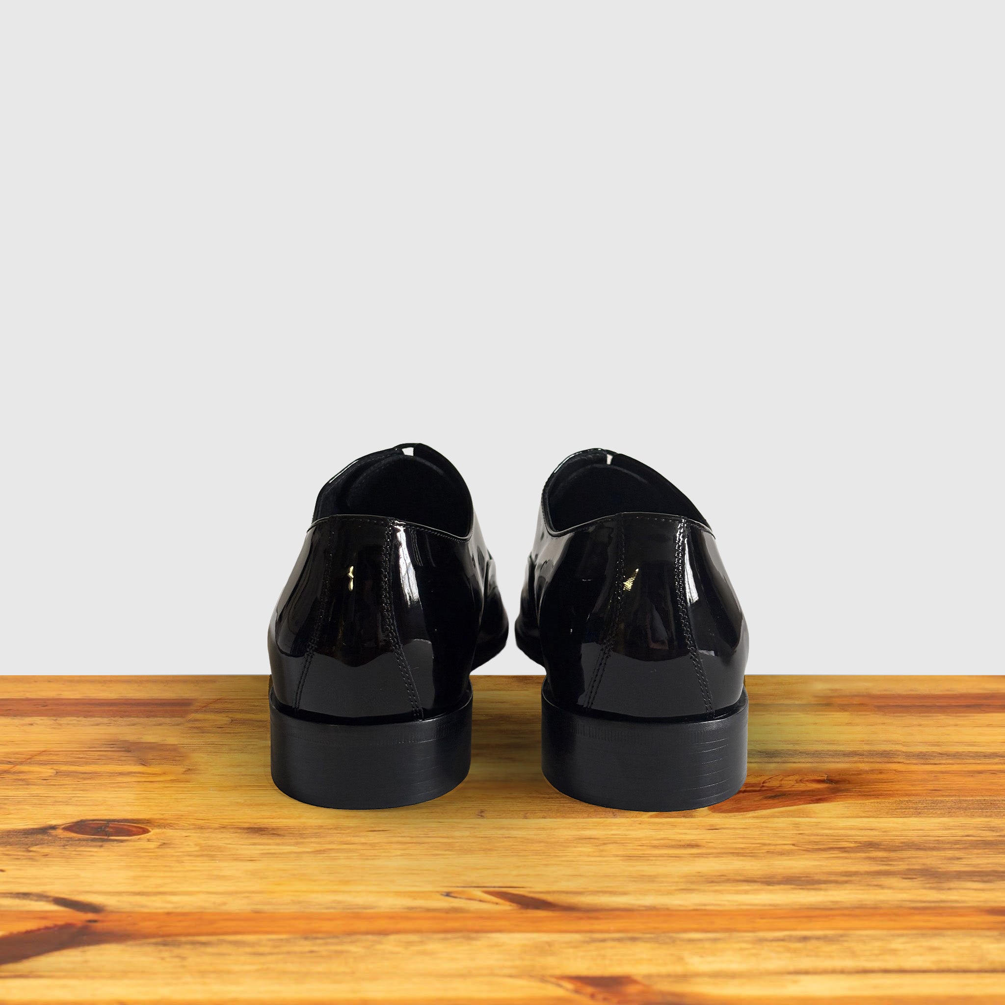 A Pair of Black patent leather dress shoe on a wooden surface with a light gray background