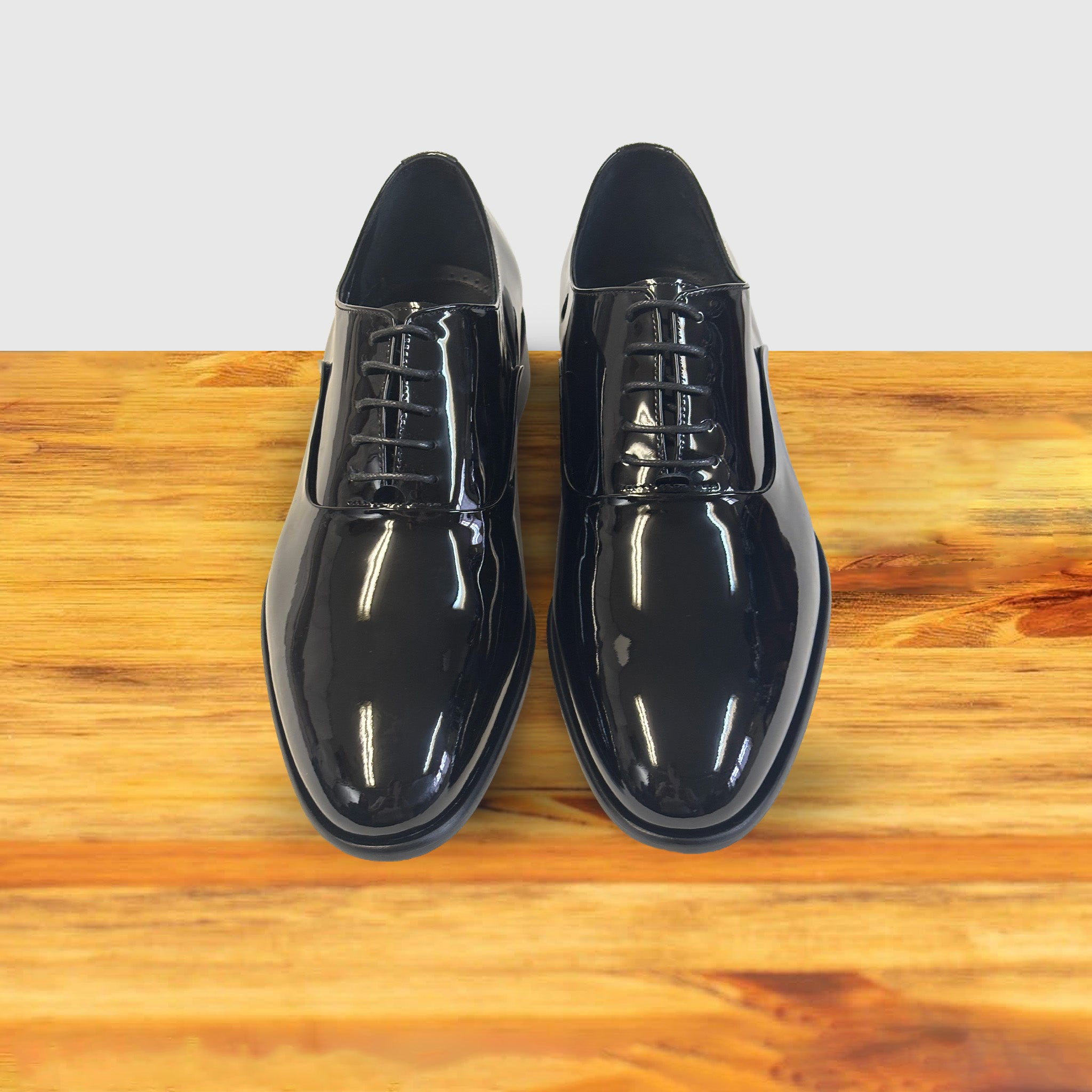 A Pair of Black patent leather dress shoe on a wooden surface with a light gray background
