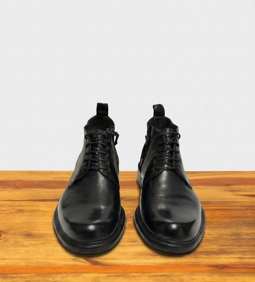 Pair of black leather boots on a wooden surface with a light gray background