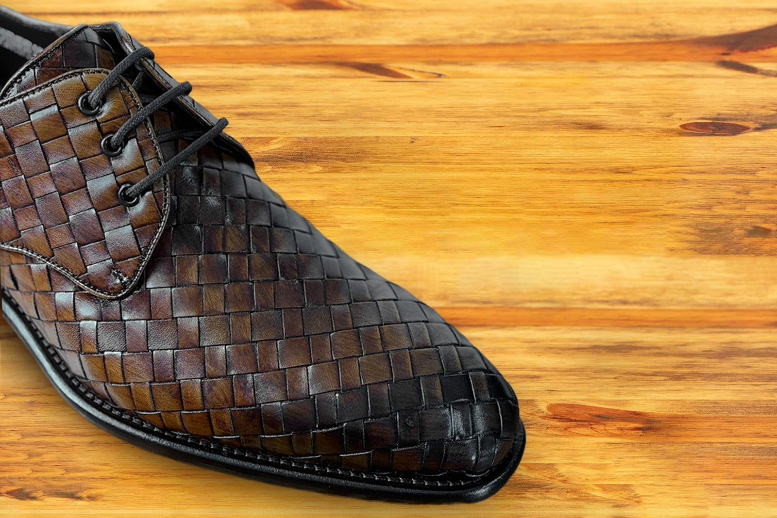 Brown woven leather shoe on a wooden surface
