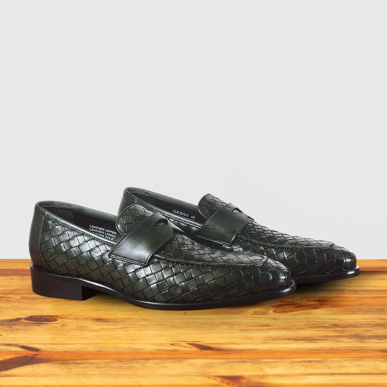 A pair of Green woven loafer shoe on a wooden surface with a light gray background