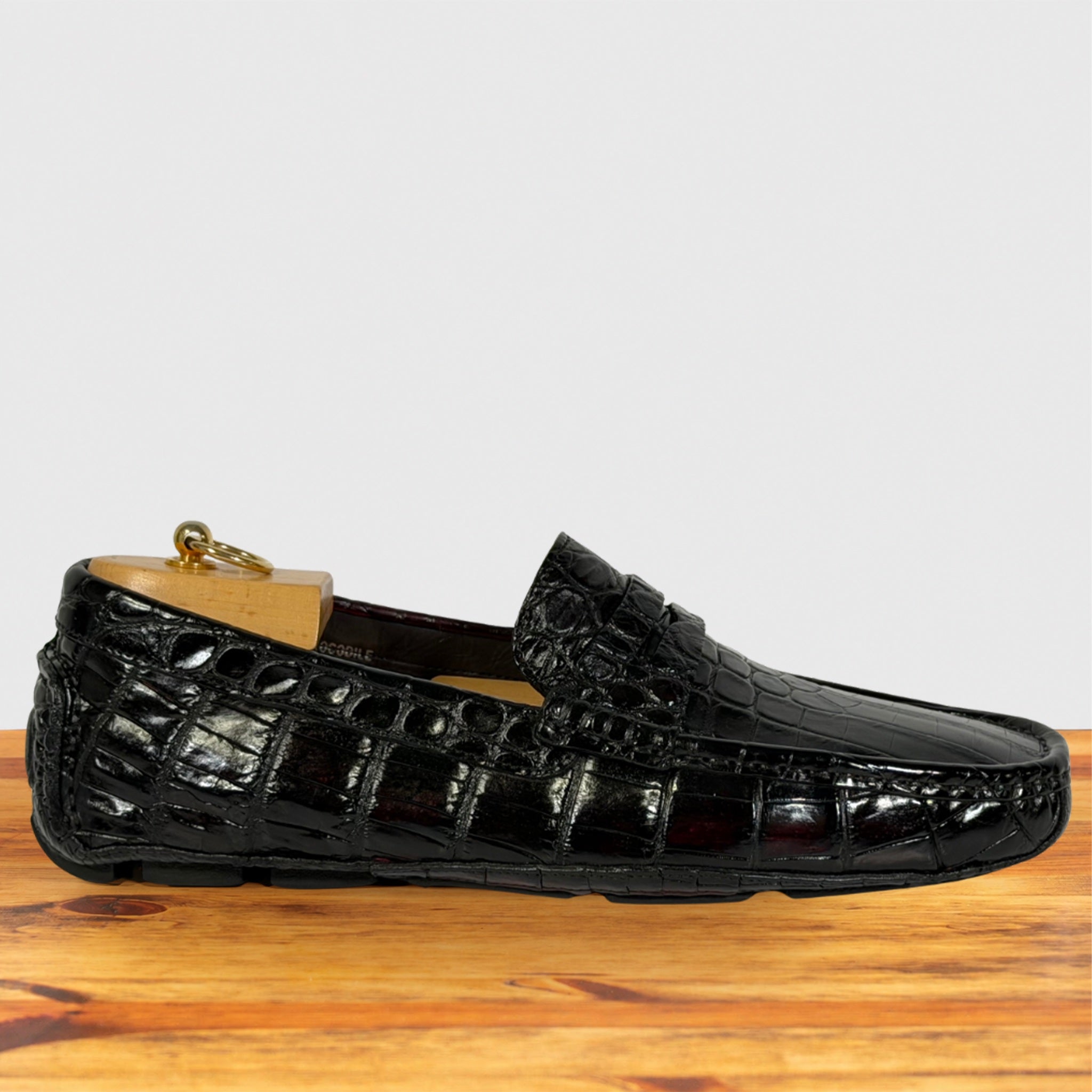 A single burgundy Genuine Crocodile loafer shoe displayed on a wooden surface against a light gray background.