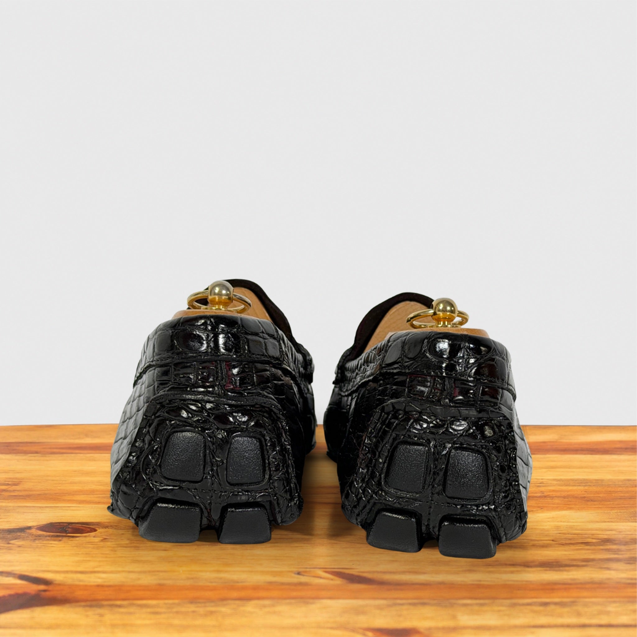 A pair of burgundy Genuine Crocodile loafers with block soles , shown from the back on a wooden surface against a light gray background.