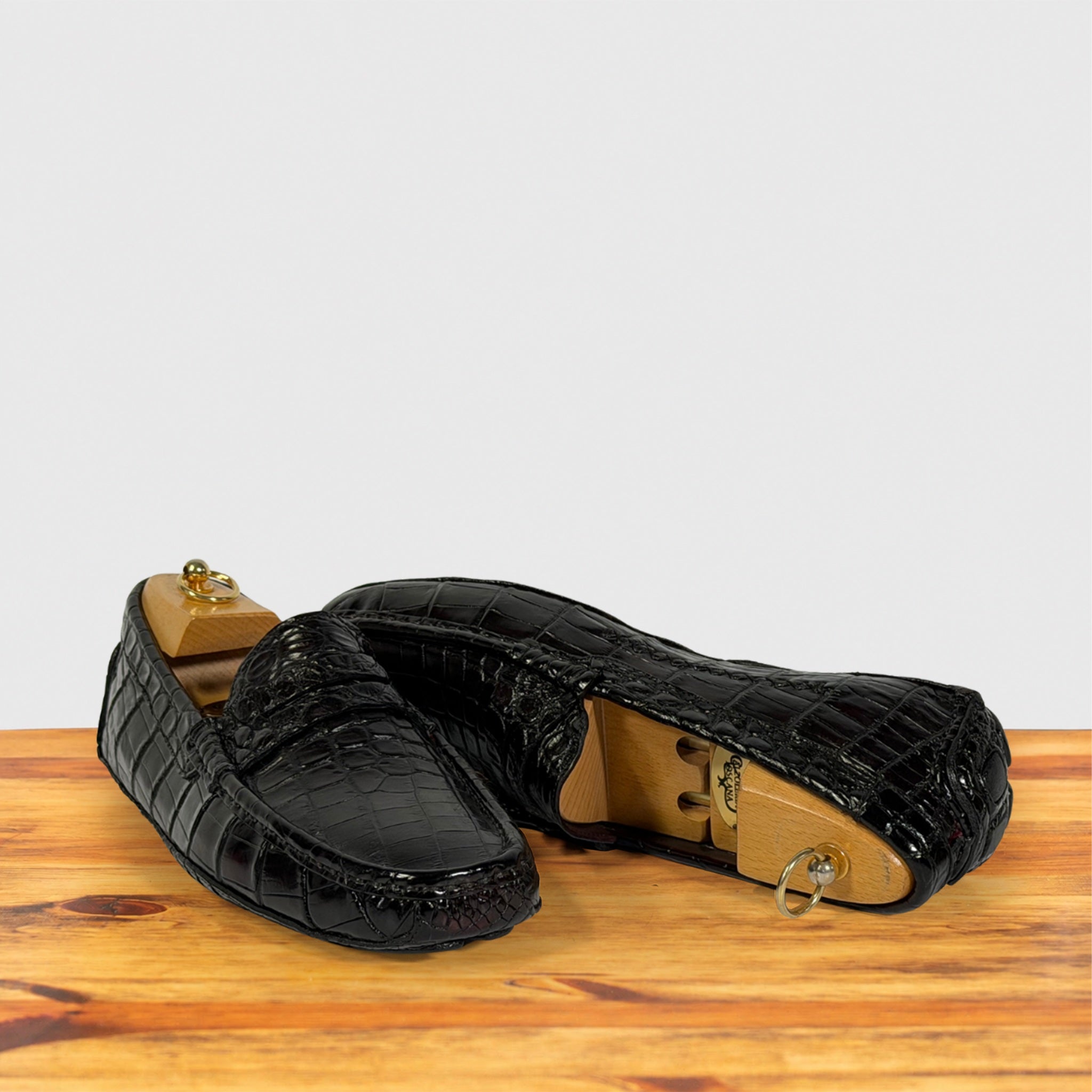 A pair of burgundy Genuine Crocodile leather loafers displayed on a wooden surface against a light gray background.