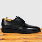 A graphite leather lace-up dress shoe with a rugged black sole, displayed on a wooden surface against a light gray background.