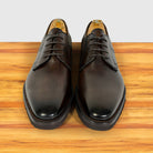 A pair of moor leather oxford dress shoes with brogue detailing, displayed on a wooden surface against a light gray background.