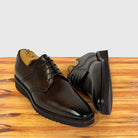 A pair of moor leather lace-up dress shoes with brogue detailing, displayed on a wooden surface against a light gray background.