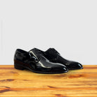 A Pair of Black shiny dress shoe on a wooden surface with a light gray background