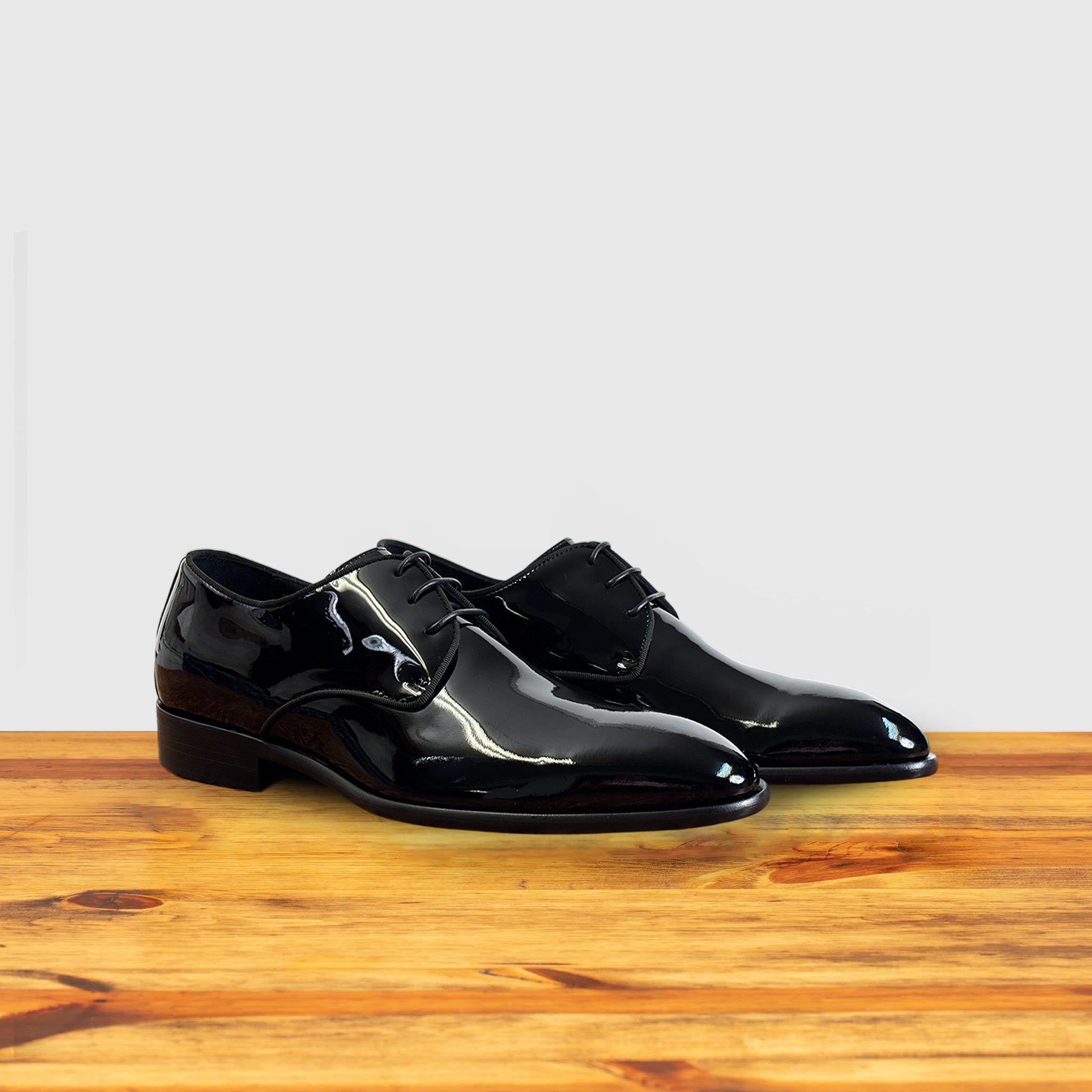A Pair of Black shiny dress shoe on a wooden surface with a light gray background