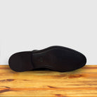 Outsole of Black shiny dress shoe on a wooden surface with a light gray background