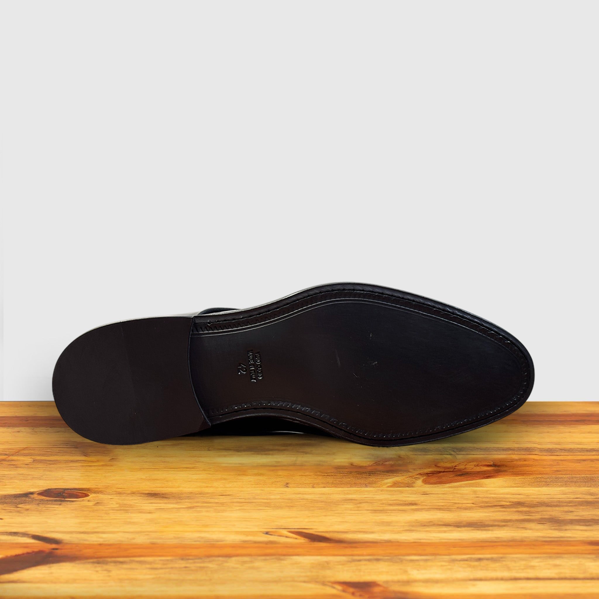Outsole of Black shiny dress shoe on a wooden surface with a light gray background