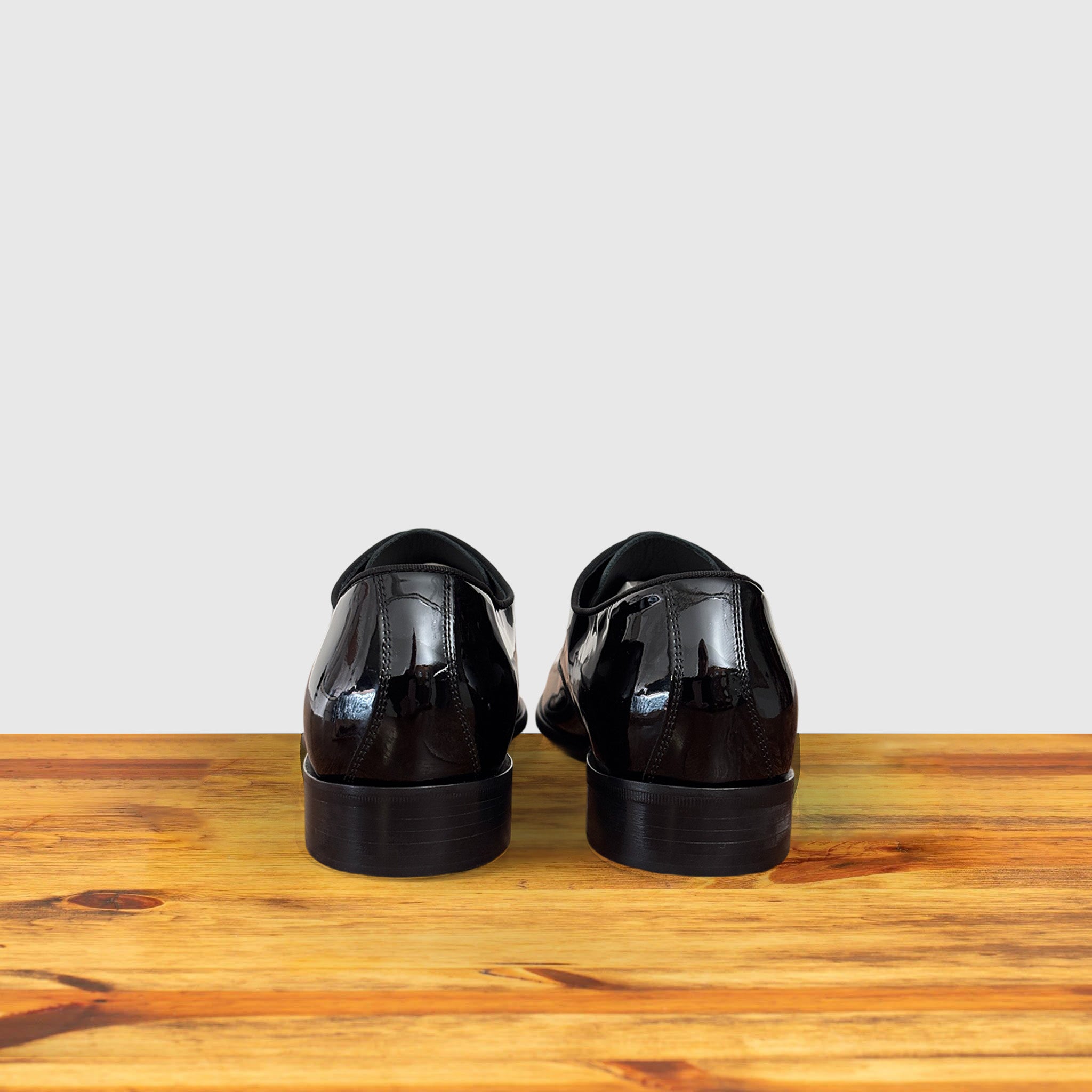 A Pair of Black shiny dress shoe on a wooden surface with a light gray background