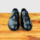 A Pair of Black shiny dress shoe on a wooden surface with a light gray background