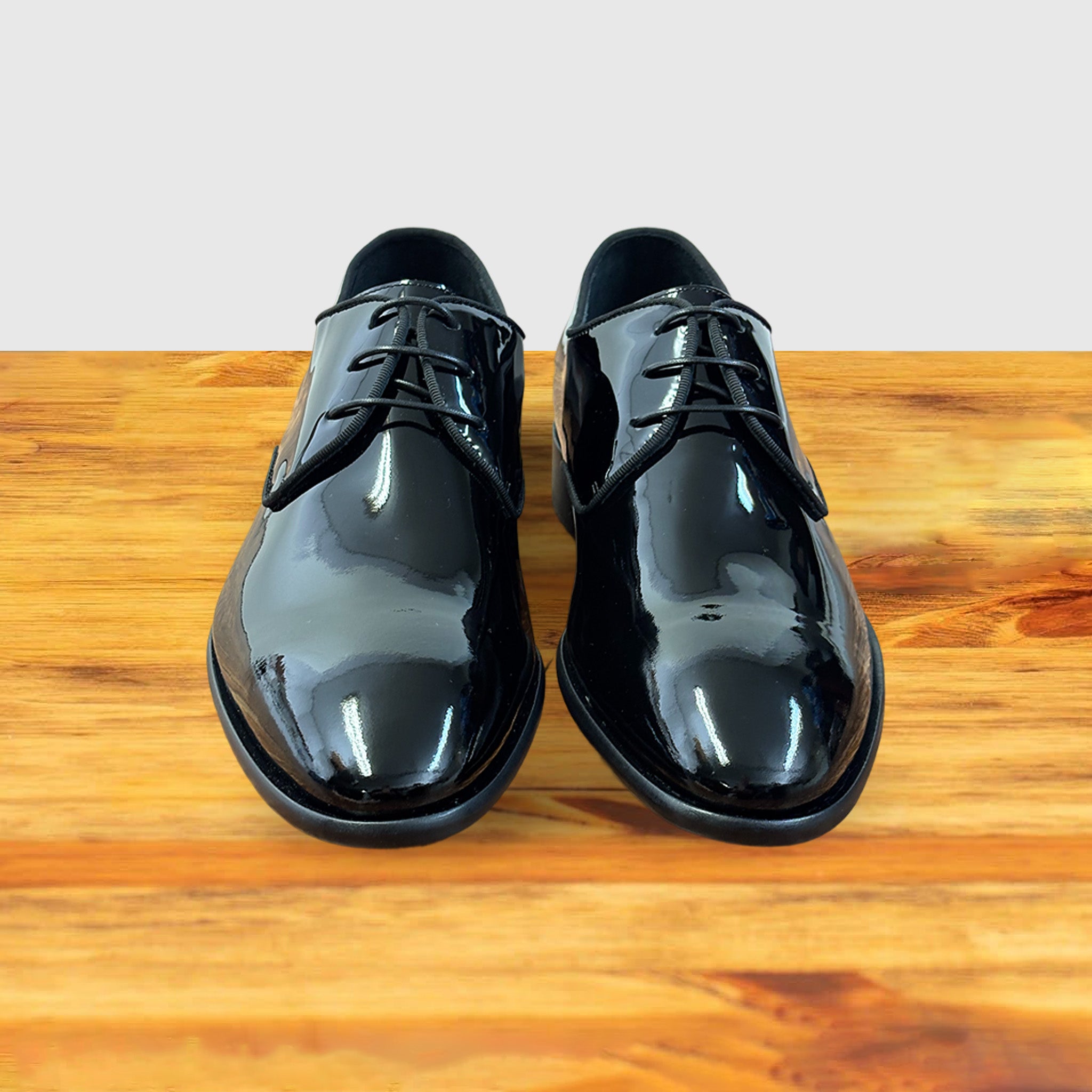 A Pair of Black shiny dress shoe on a wooden surface with a light gray background