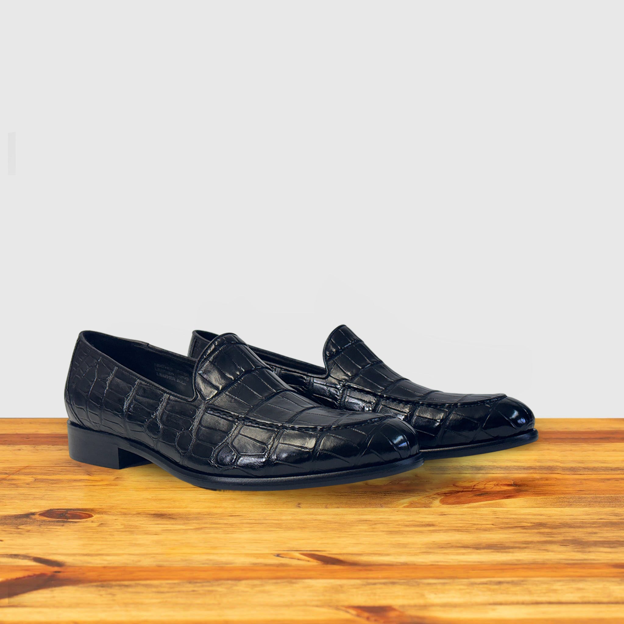 A pair of crocodile loafer shoe on a wooden surface with a light gray background