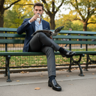 Man in a suit sitting on a park bench reading a newspaper and drinking coffee wear Black crocodile loafer shoe.