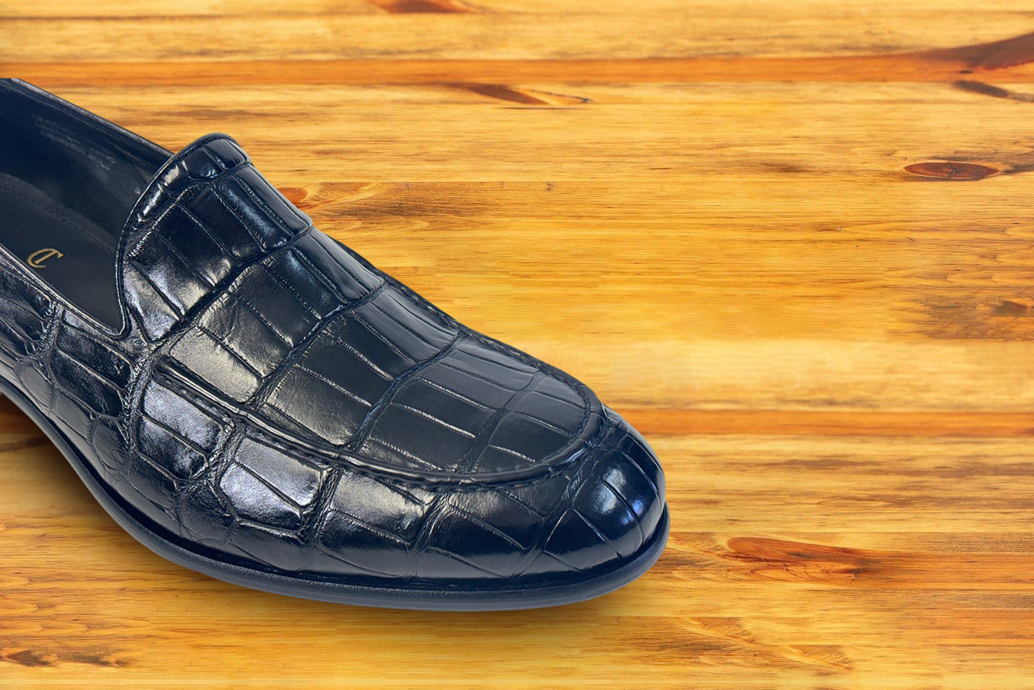 Black crocodile loafer shoe on a wooden surface.
