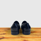A pair of Black crocodile loafer shoe on a wooden surface with a light gray background