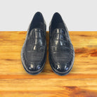 A pair of Black crocodile loafer shoe on a wooden surface with a light gray background