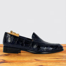 A single dark navy blue crocodile-embossed leather loafer shown in profile on a wooden surface against a light gray background.