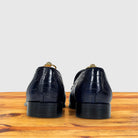 A pair of dark navy blue crocodile-embossed leather loafers shown from the back, resting on a wooden surface against a light gray background.