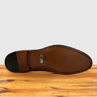 The underside of a leather dress shoe sole, showing the VAMP brand logo and black heel cap, resting on a wooden surface against a light gray background.