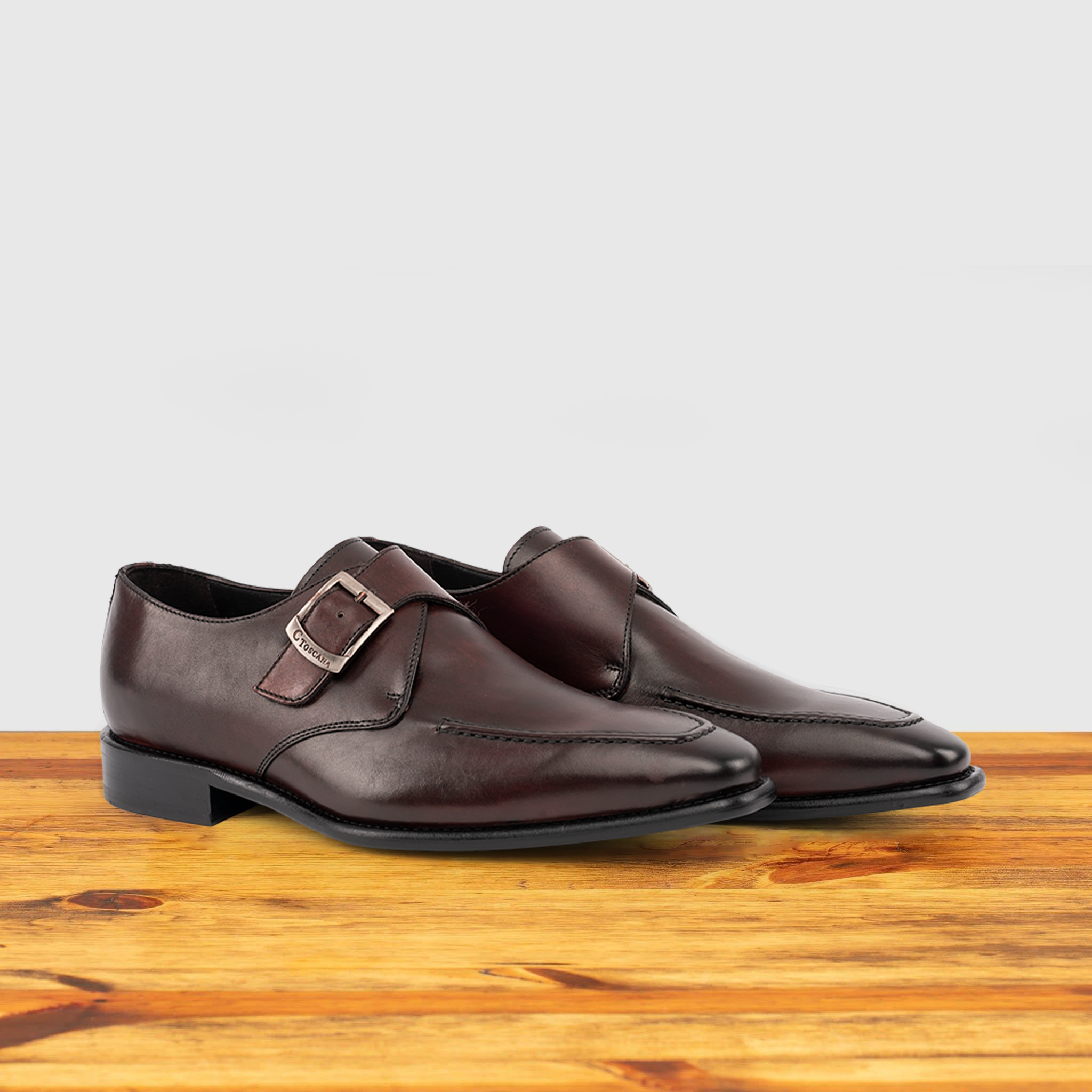 A Pair of burgundy monk strap shoe with a silver buckle on a wooden surface