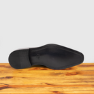 Outsole of burgundy monk strap shoe with a silver buckle on a wooden surface