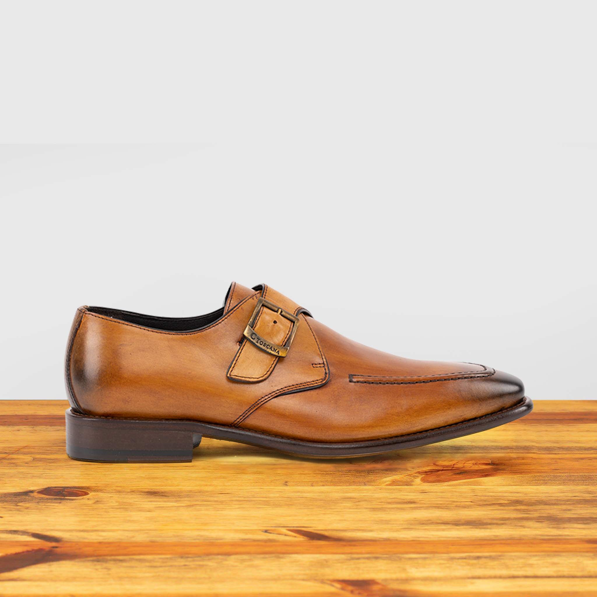 Caramel leather dress shoe with a buckle on a wooden surface