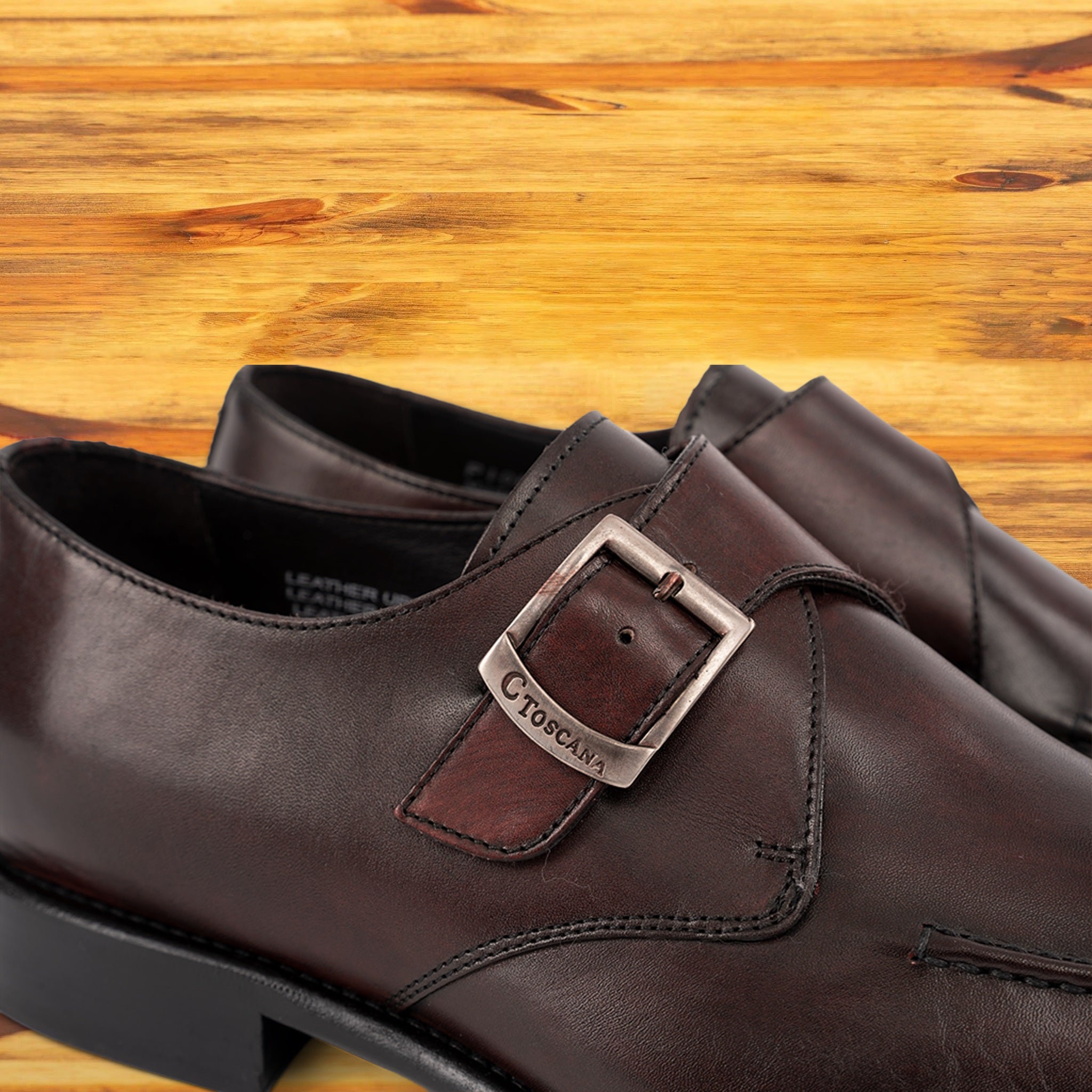 A burgundy monk strap shoe with a silver buckle on a wooden surface