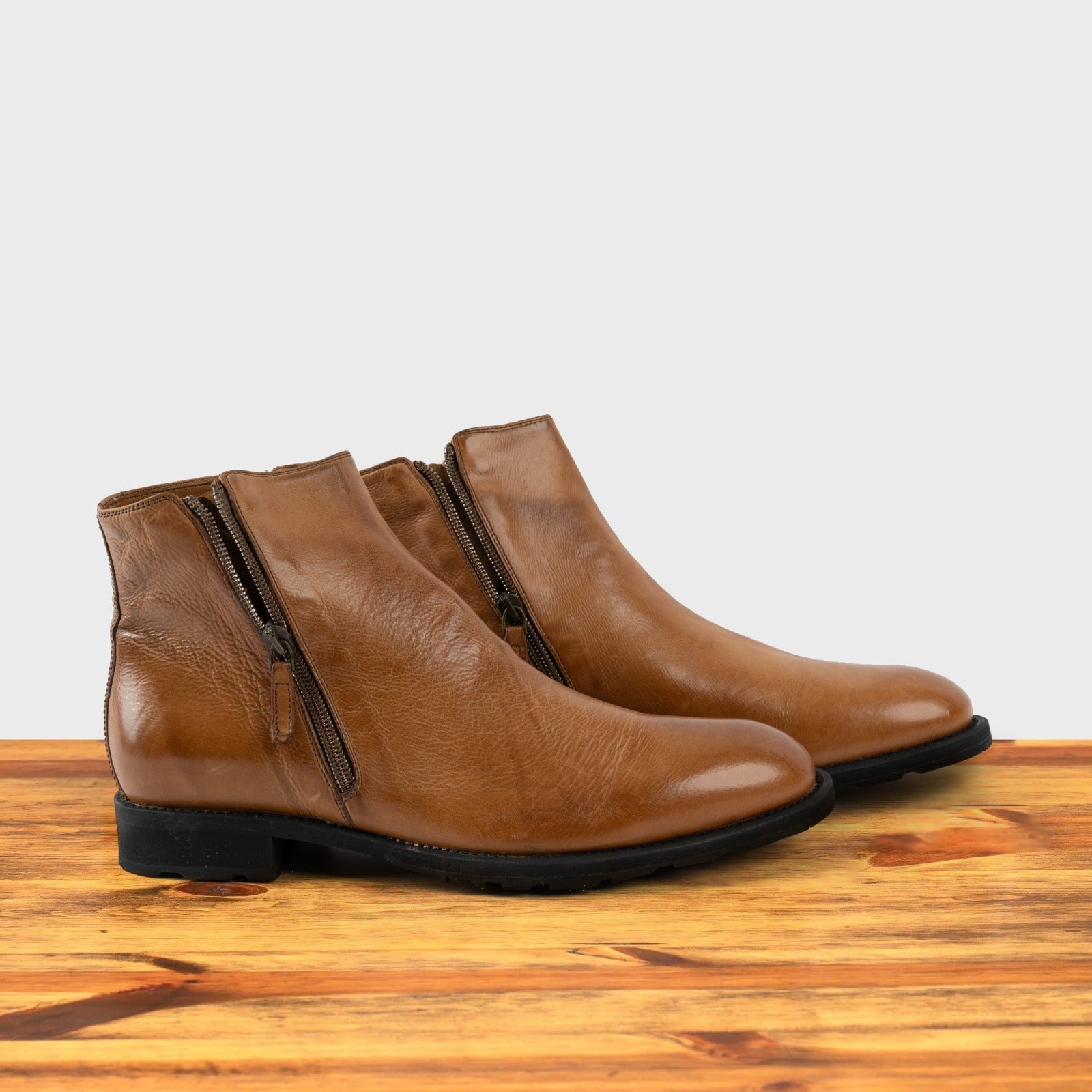 A Pair of brick leather ankle boot with a double zipper design on the side, placed on a wooden surface.