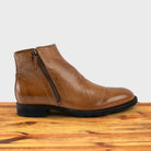 A brick leather ankle boot with a double zipper design on the side, placed on a wooden surface.