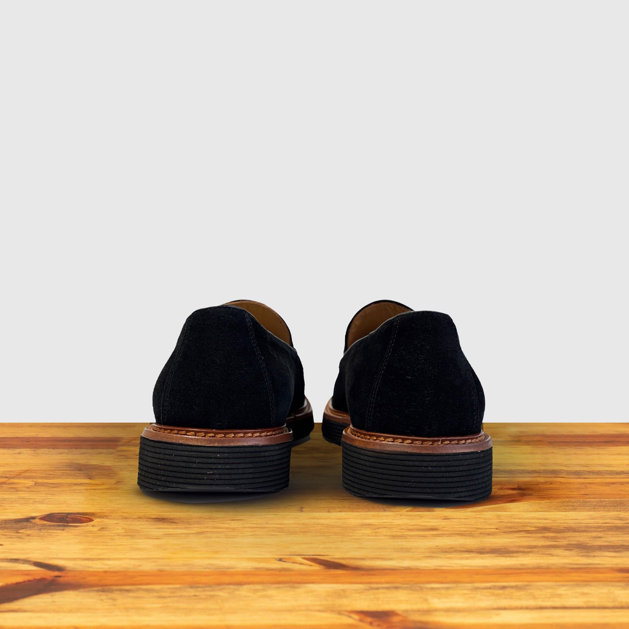 A pair of Black Venetian loafer with a rubber sole positioned on a wooden surface.