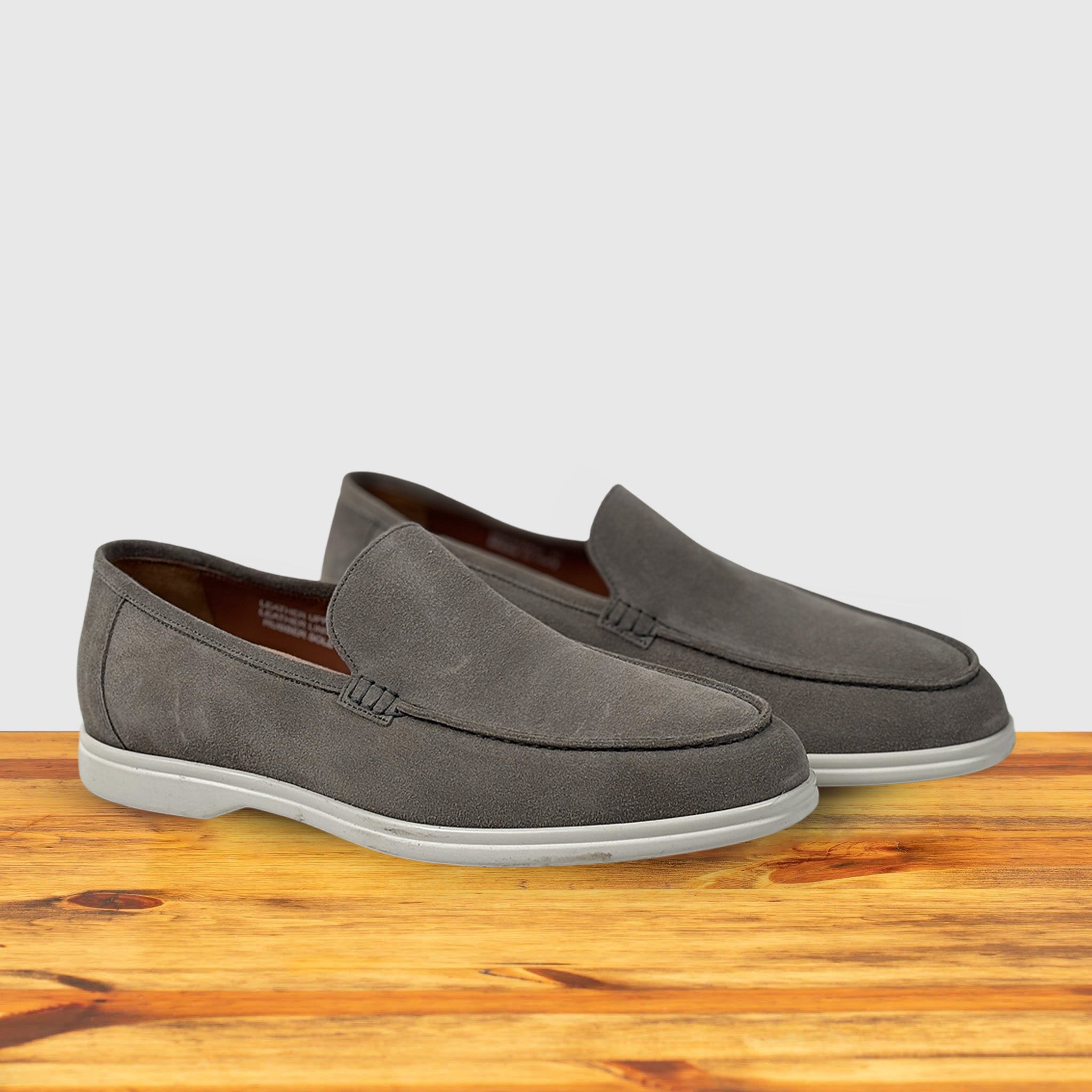 Gray loafer shoes on a wooden surface with a light gray background