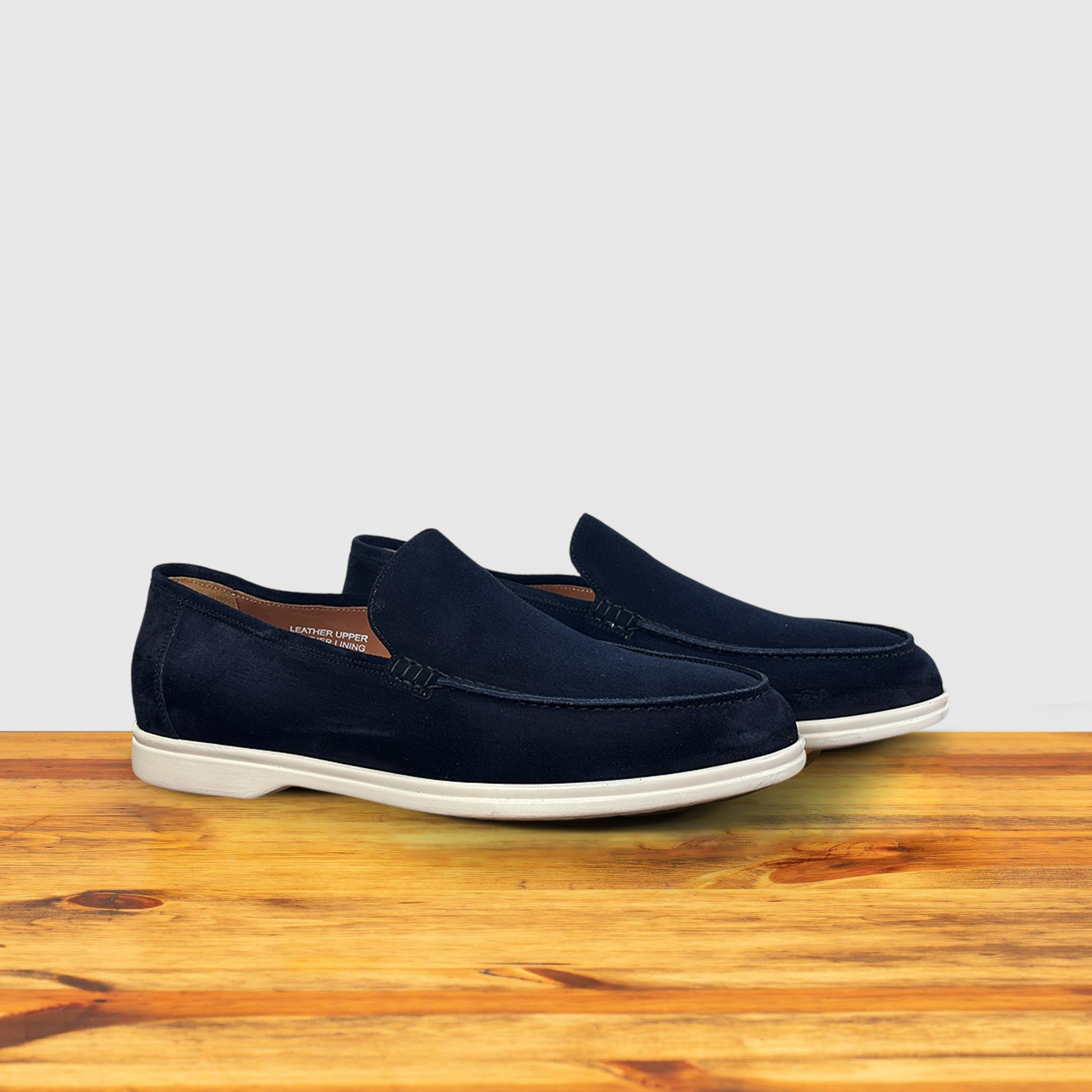 A Navy Blue suede loafer with  white sole, displayed on a wooden surface.