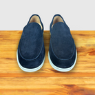 A Pair of Navy Blue suede loafer with  white sole, displayed on a wooden surface.