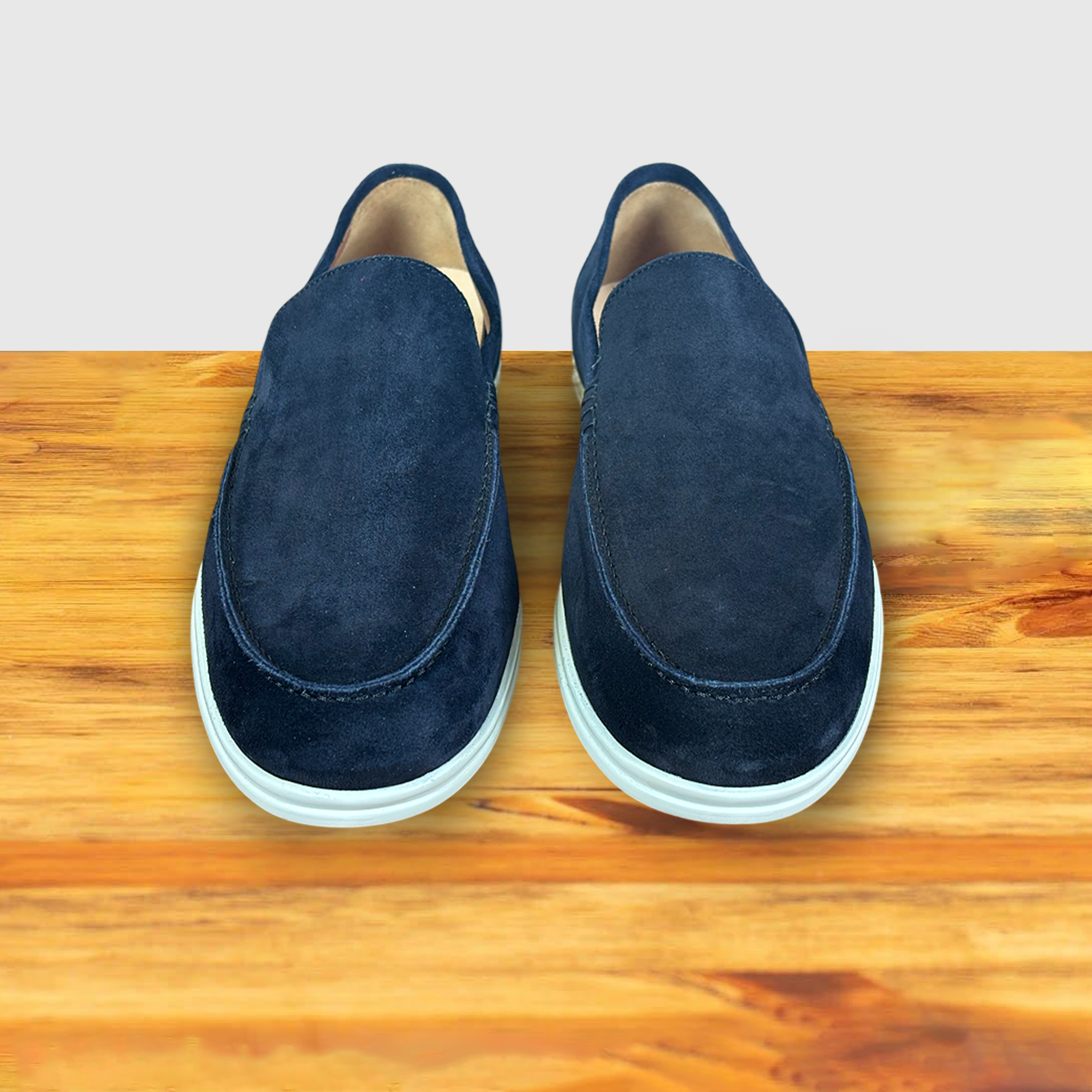 A Pair of Navy Blue suede loafer with  white sole, displayed on a wooden surface.