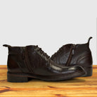 Pair of dark brown leather boots on a wooden surface with a light gray background