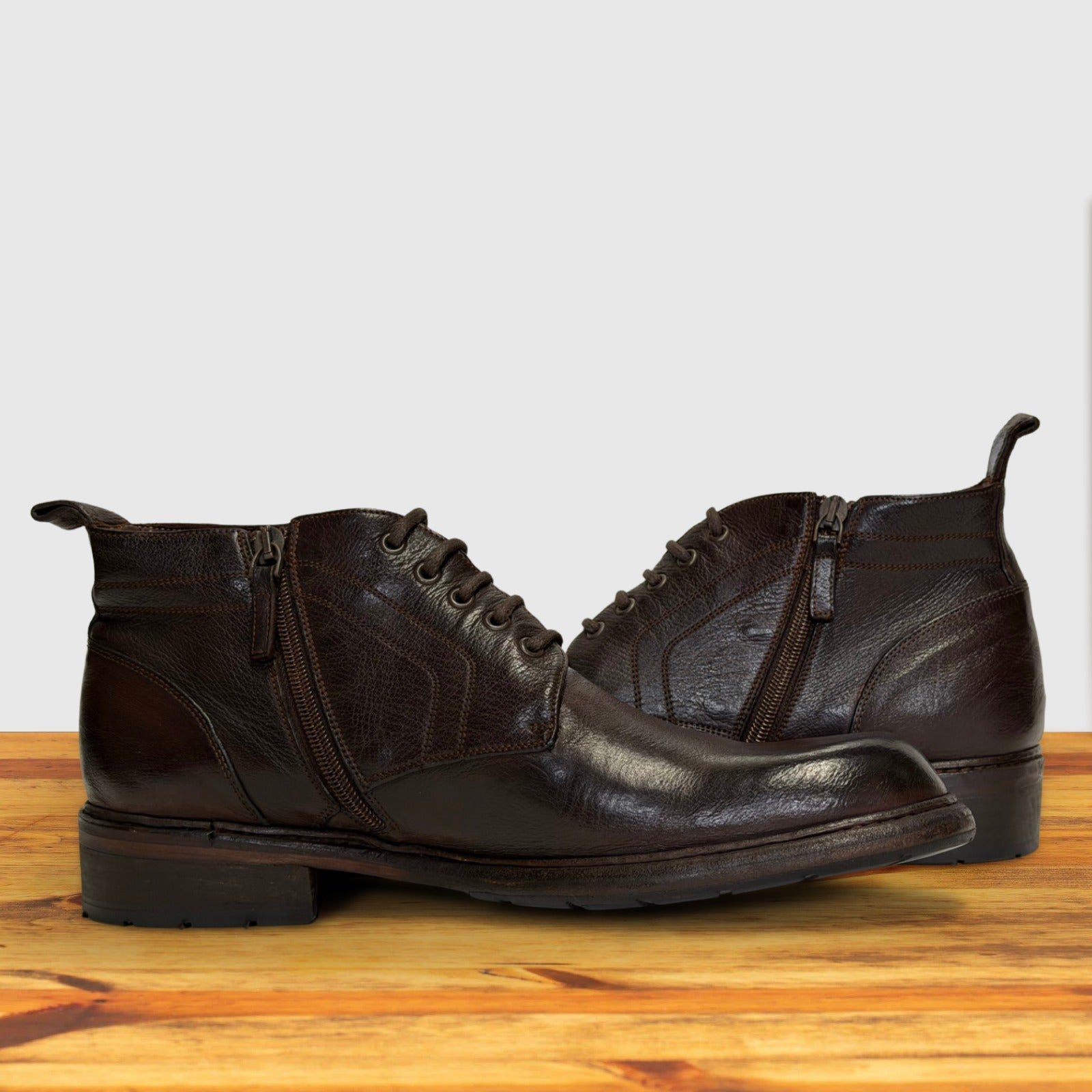 Pair of dark brown leather boots on a wooden surface with a light gray background